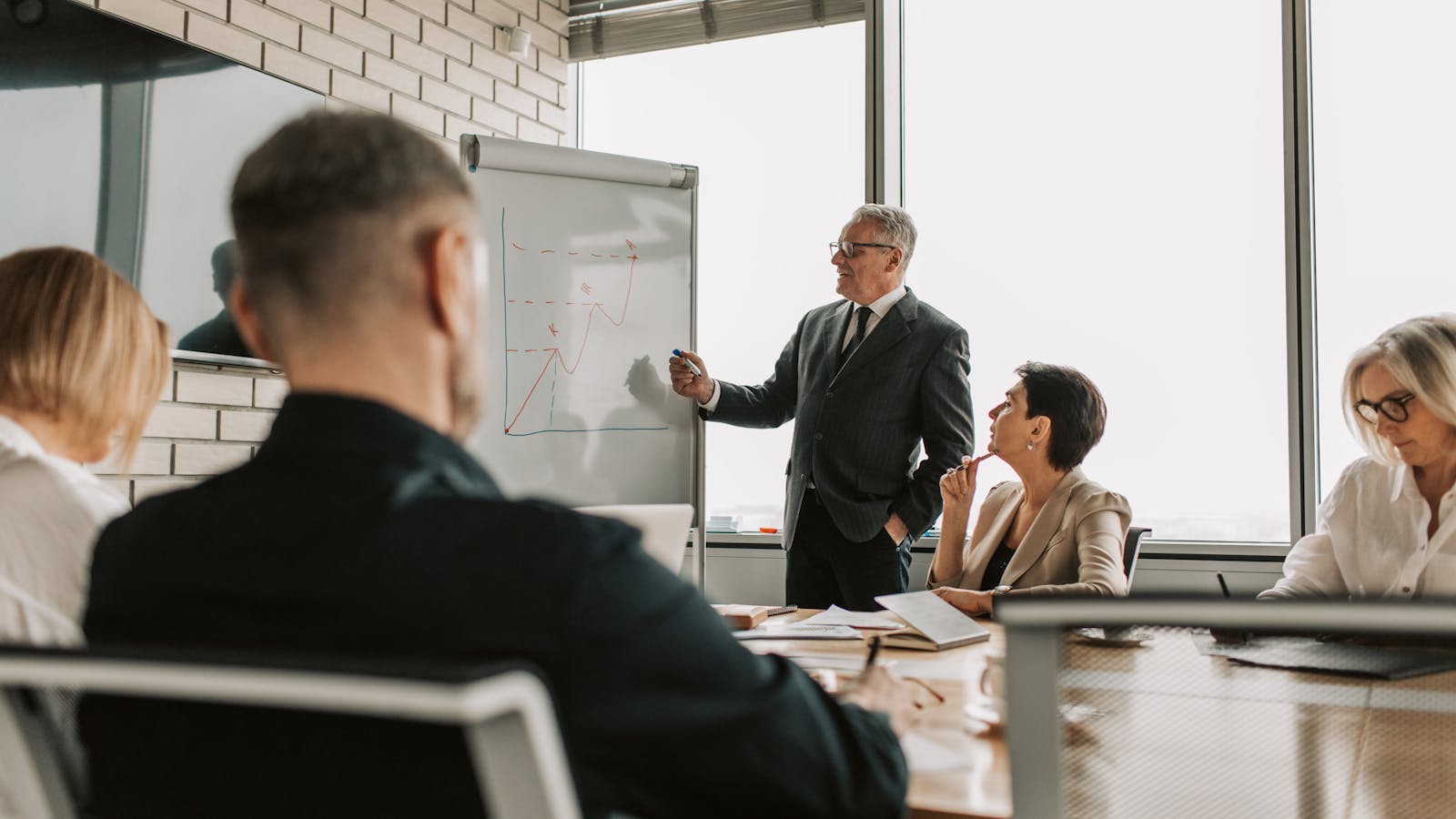 A sales leader at a glass desk reviewing pipeline metrics with a small team in the background